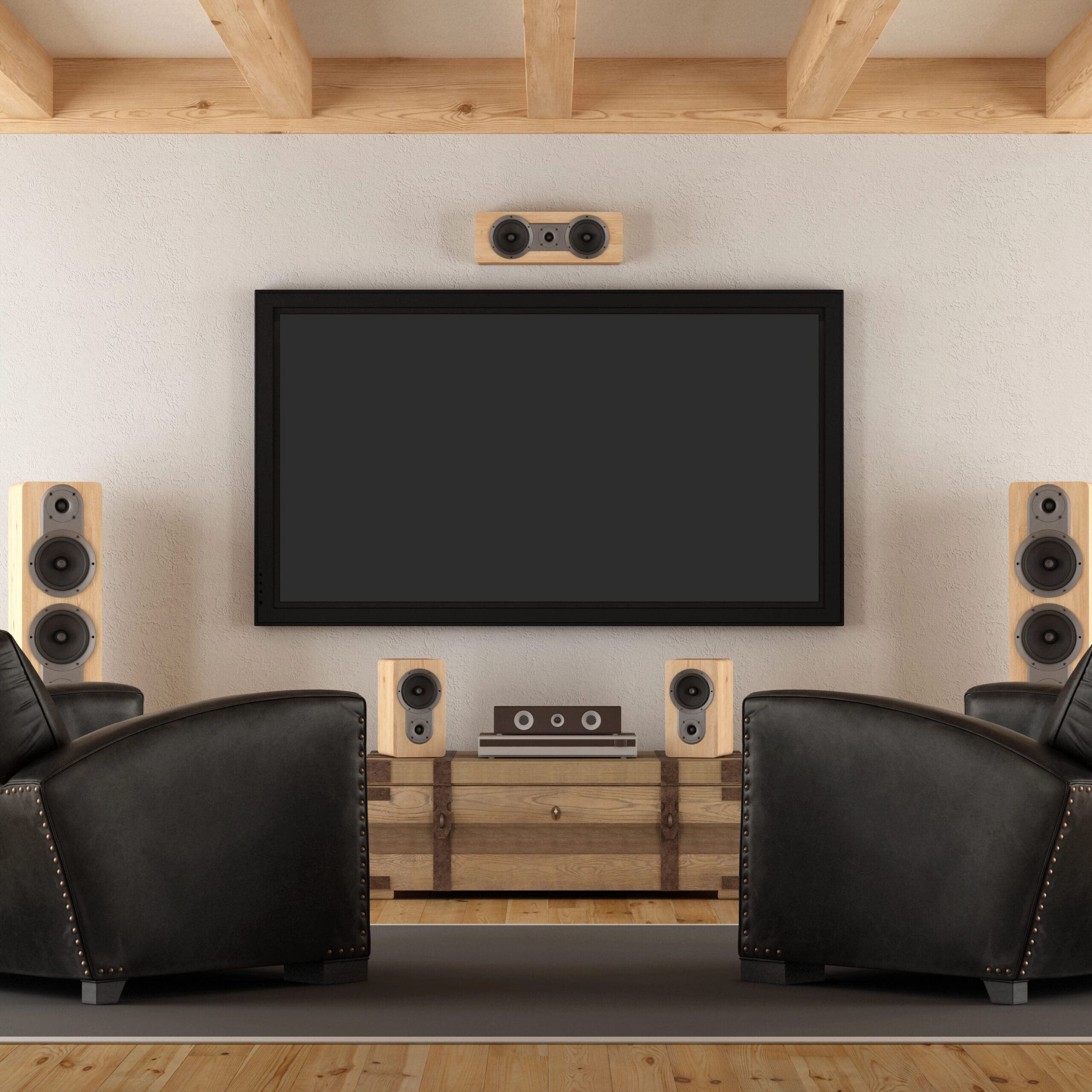 Home theater setup with two black leather recliners, a large flatscreen TV, six speakers, and two pendant lights on a wooden floor with exposed beam ceiling.