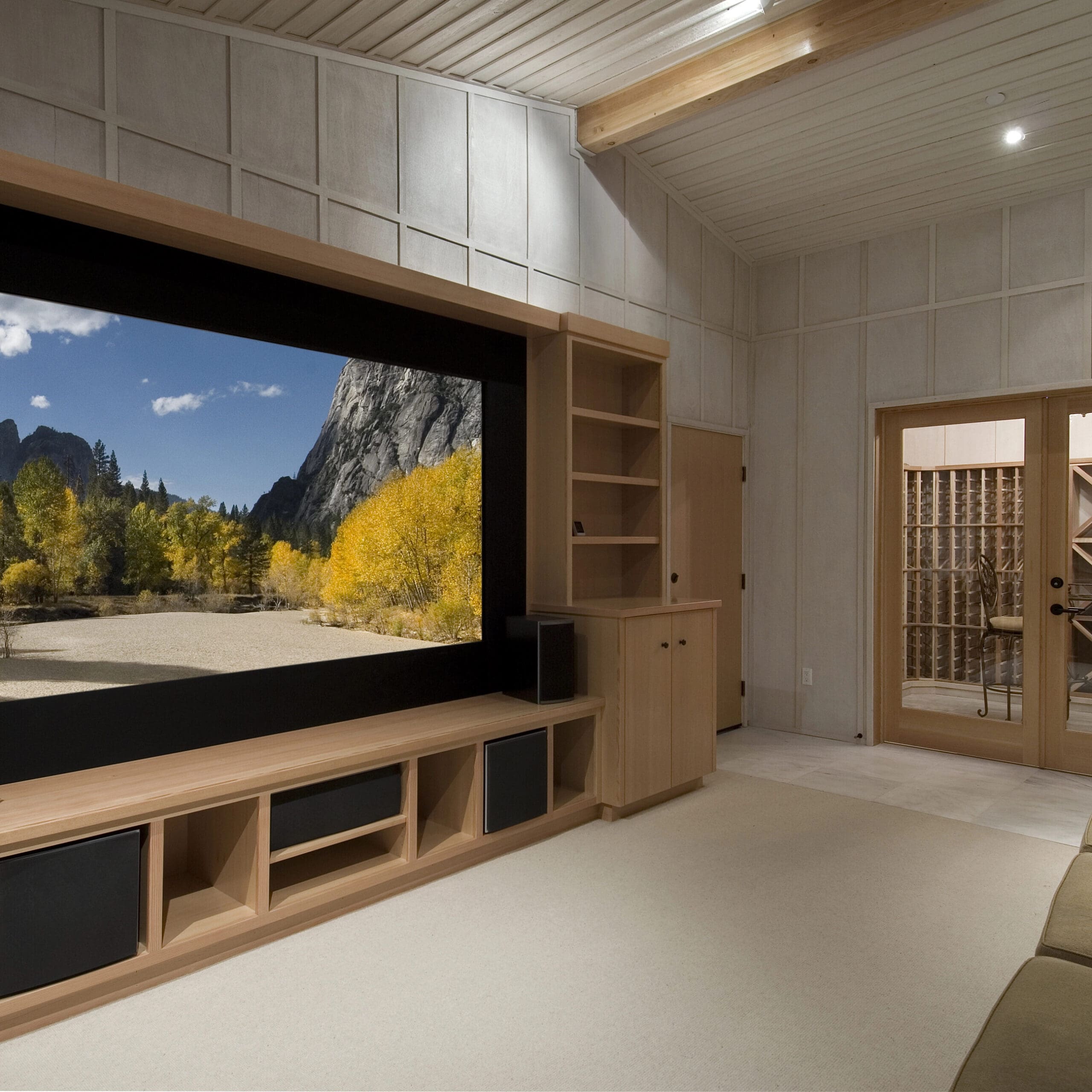 A home theater room featuring a large screen displaying a scenic landscape, wooden shelves, a sofa, and French doors with glass panels.