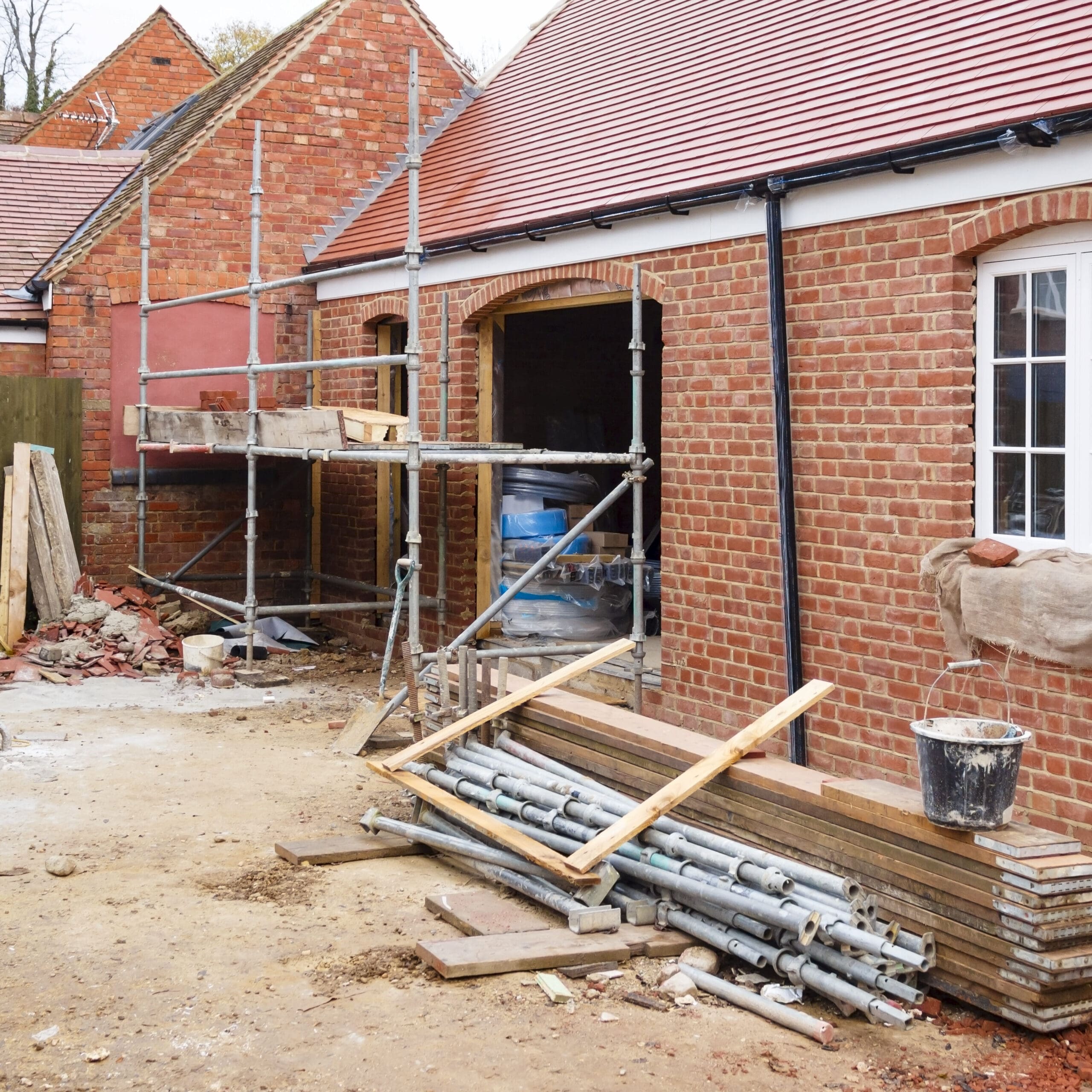 Construction site of a brick building with scaffolding, a cement mixer, and various construction materials.