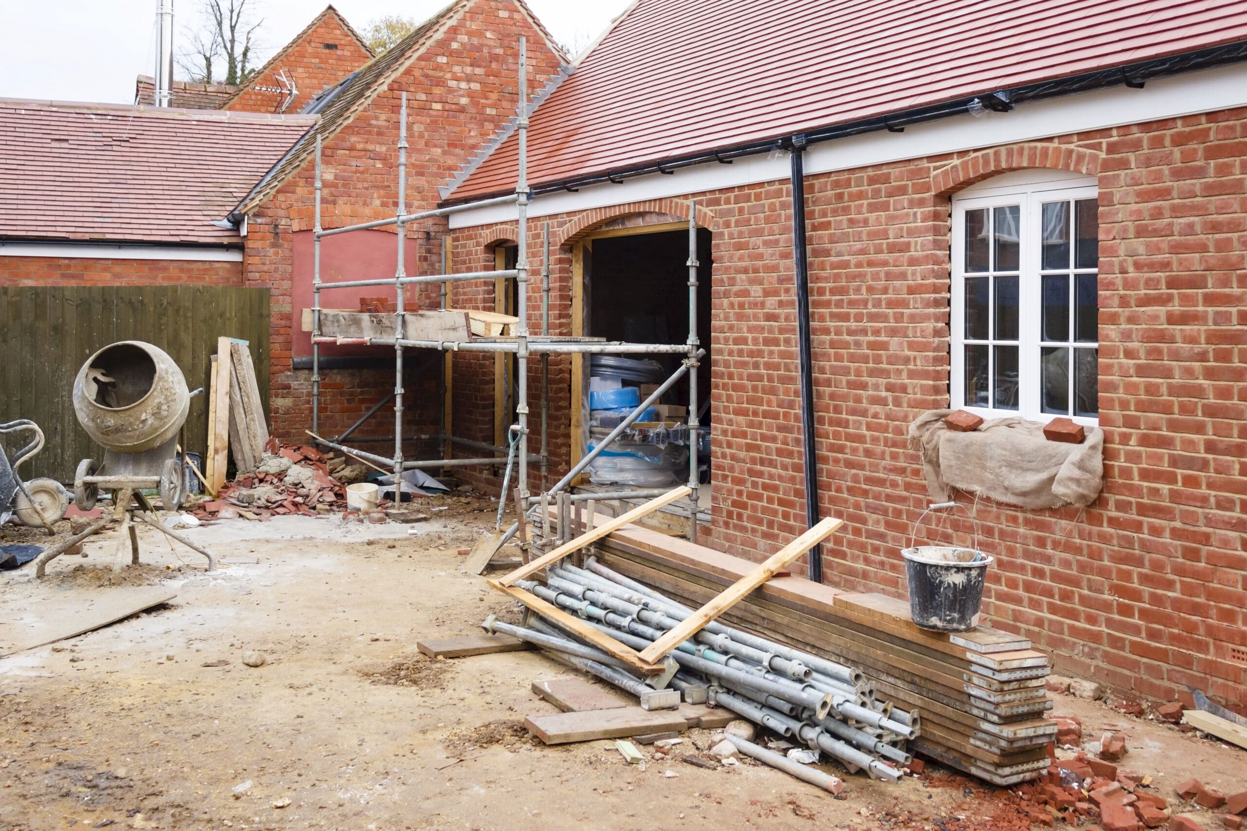 Construction site of a brick building with scaffolding, a cement mixer, and various construction materials.