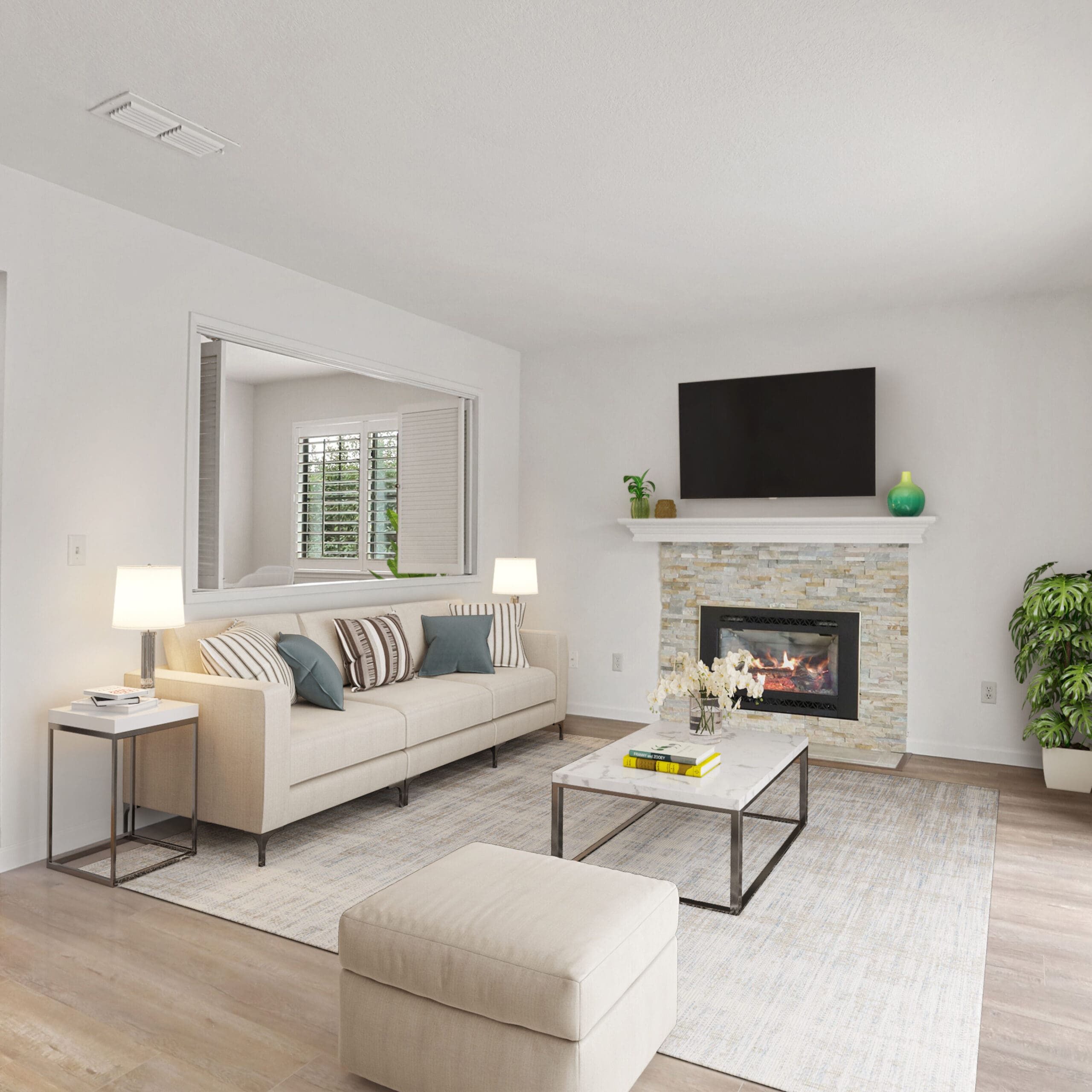 A modern living room with a beige sofa, cushions, a coffee table, a fireplace, and a wall-mounted TV. There’s a large window, glass doors, and a side view of a dining area and office space.