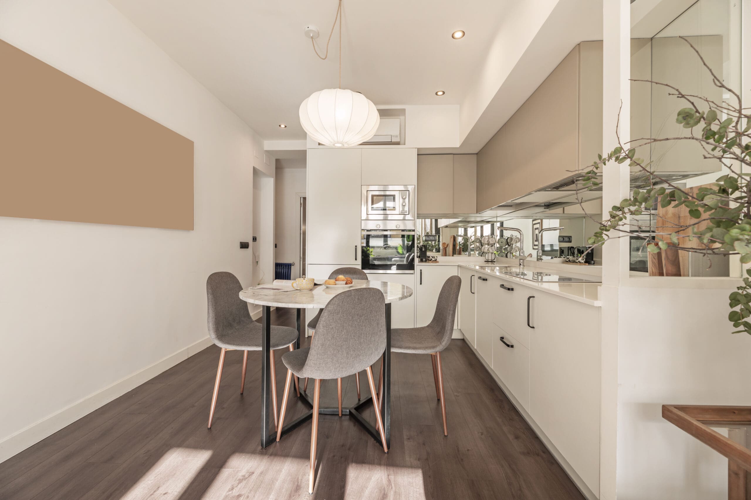 Modern kitchen and dining area with a round table, four gray chairs, white cabinetry, and a large round ceiling light.