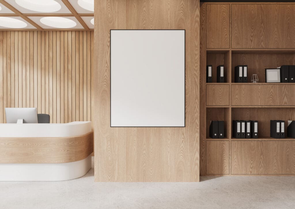 Modern office reception area with a blank vertical poster on a wooden wall, a white curved desk, and shelves holding black binders and decor items.