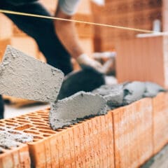 A construction worker spreads mortar on bricks with a trowel while building a brick wall.