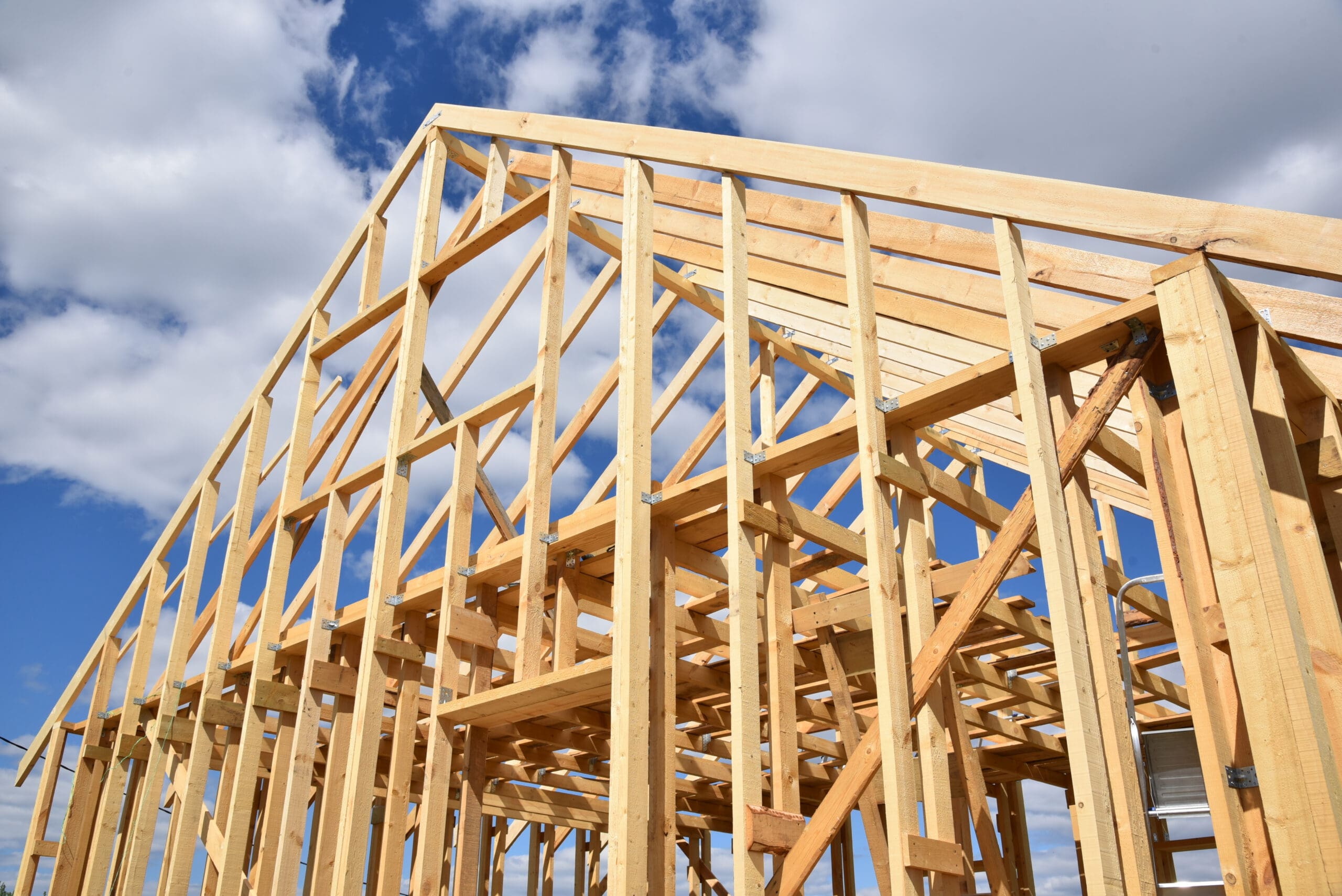 Wooden frame of a house under construction against a blue sky with clouds.