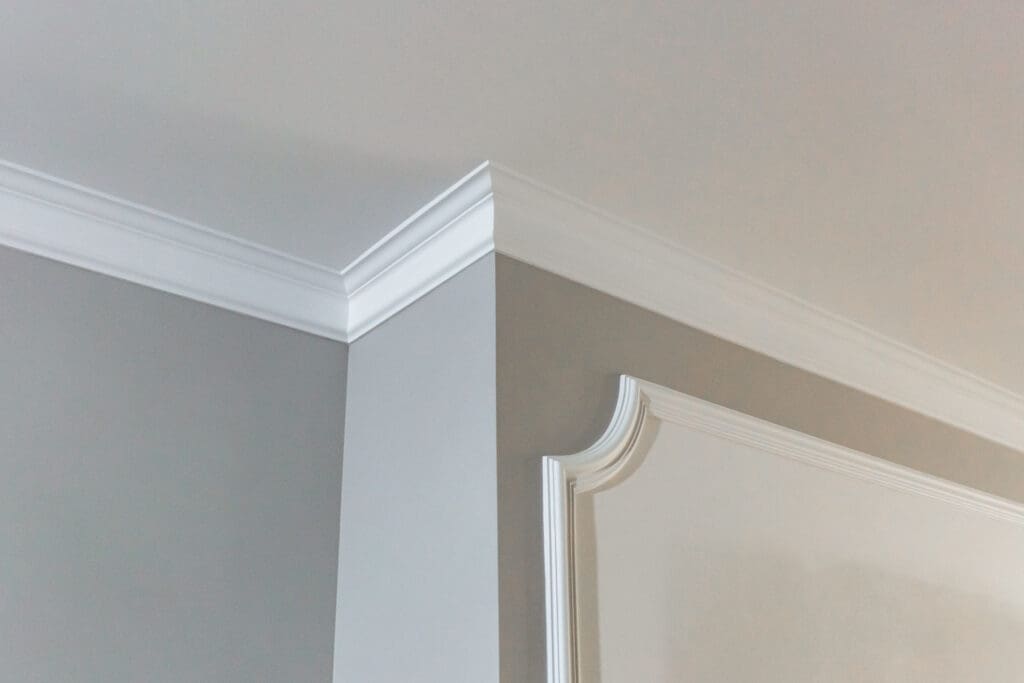 White crown molding on a gray and white interior wall corner, featuring detailed trim and a smooth, clean finish.