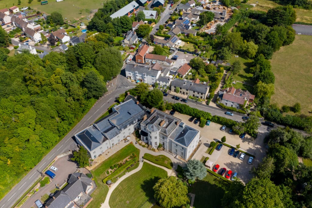Aerial view of a residential neighborhood with houses, a large building with a parking lot, green lawns, trees, and roads intersecting the area.